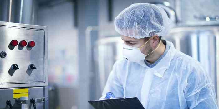 Homme portant un ÉPI inspectant une machine pour la conformité à la salubrité alimentaire